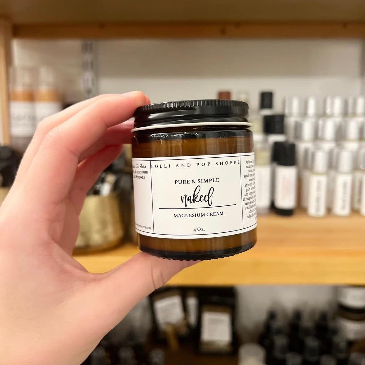 Hand holding a jar of cream labeled 'Pure & Simple' with a blurred background of shelves.