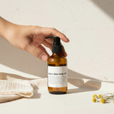 Brown bottle of 'baby's first body oil' on a beige background with a white label.
