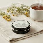 Round container of 'All Natural Calm the Cramps Salve' from Lolli and Pop Shoppe on a wooden surface.