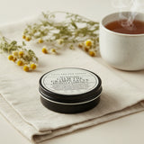 Round container of 'All Natural Calm the Cramps Salve' from Lolli and Pop Shoppe on a wooden surface.