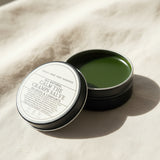 Round container of 'All Natural Calm the Cramps Salve' from Lolli and Pop Shoppe on a wooden surface.