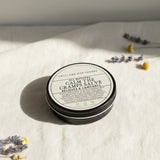 Round container of 'All Natural Calm the Cramps Salve' from Lolli and Pop Shoppe on a wooden surface.