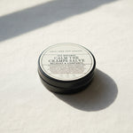 Round container of 'All Natural Calm the Cramps Salve' from Lolli and Pop Shoppe on a wooden surface.