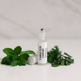 A small clear roll-on bottle labeled TARGETED COMFORT with a white cap, styled on a light marble surface with green mint and herb leaves around it.