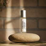 A small cylindrical bottle labeled TARGETED COMFORT stands upright on a smooth round stone against a blurred brick wall background with warm sunlight and shadows.