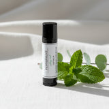 Hand holding a peppermint lip balm with a blurred background of a wooden table and rug.