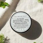 All natural peppermint pine headache salve container on a light fabric background with greenery.